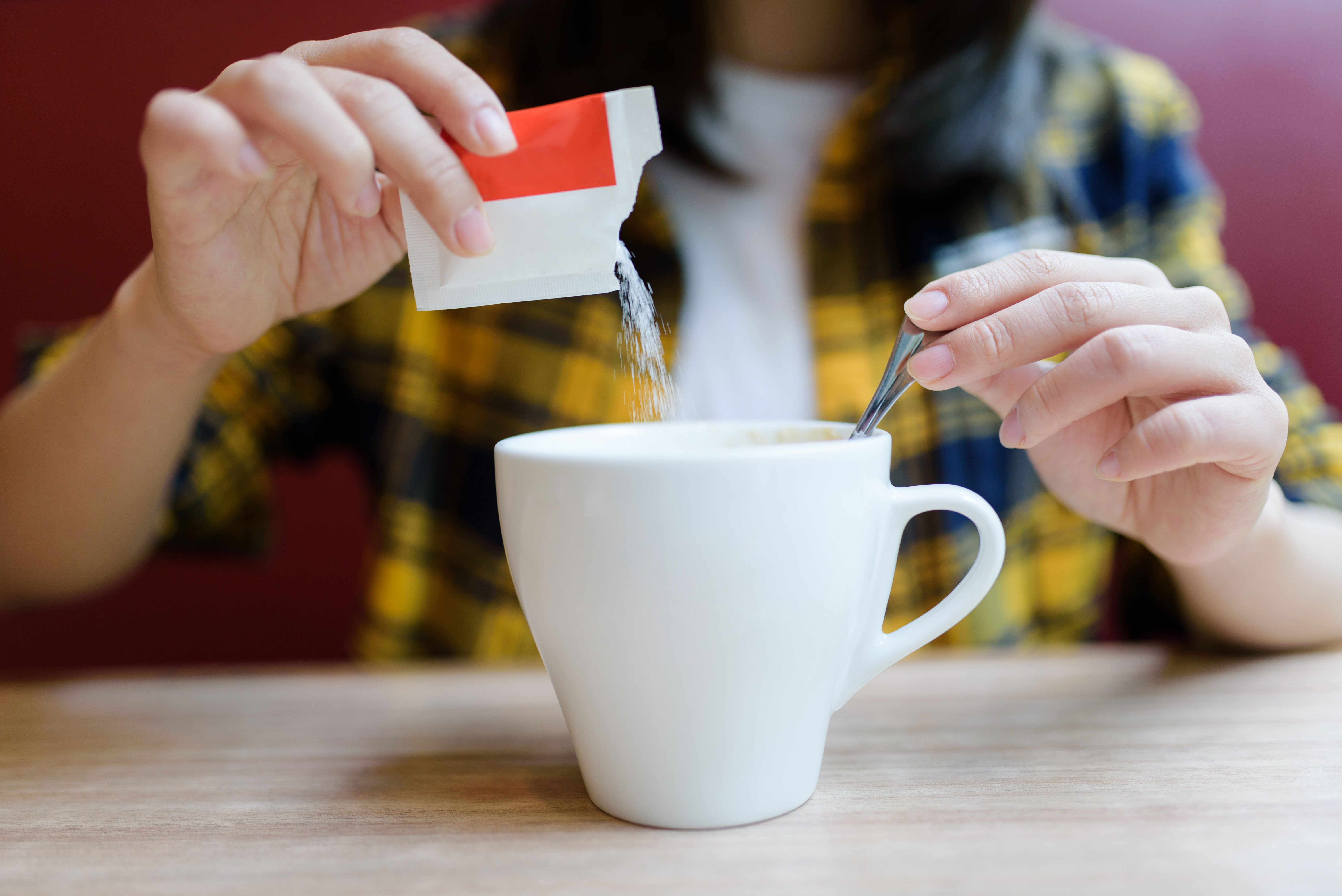Person pouring sugar into a mug