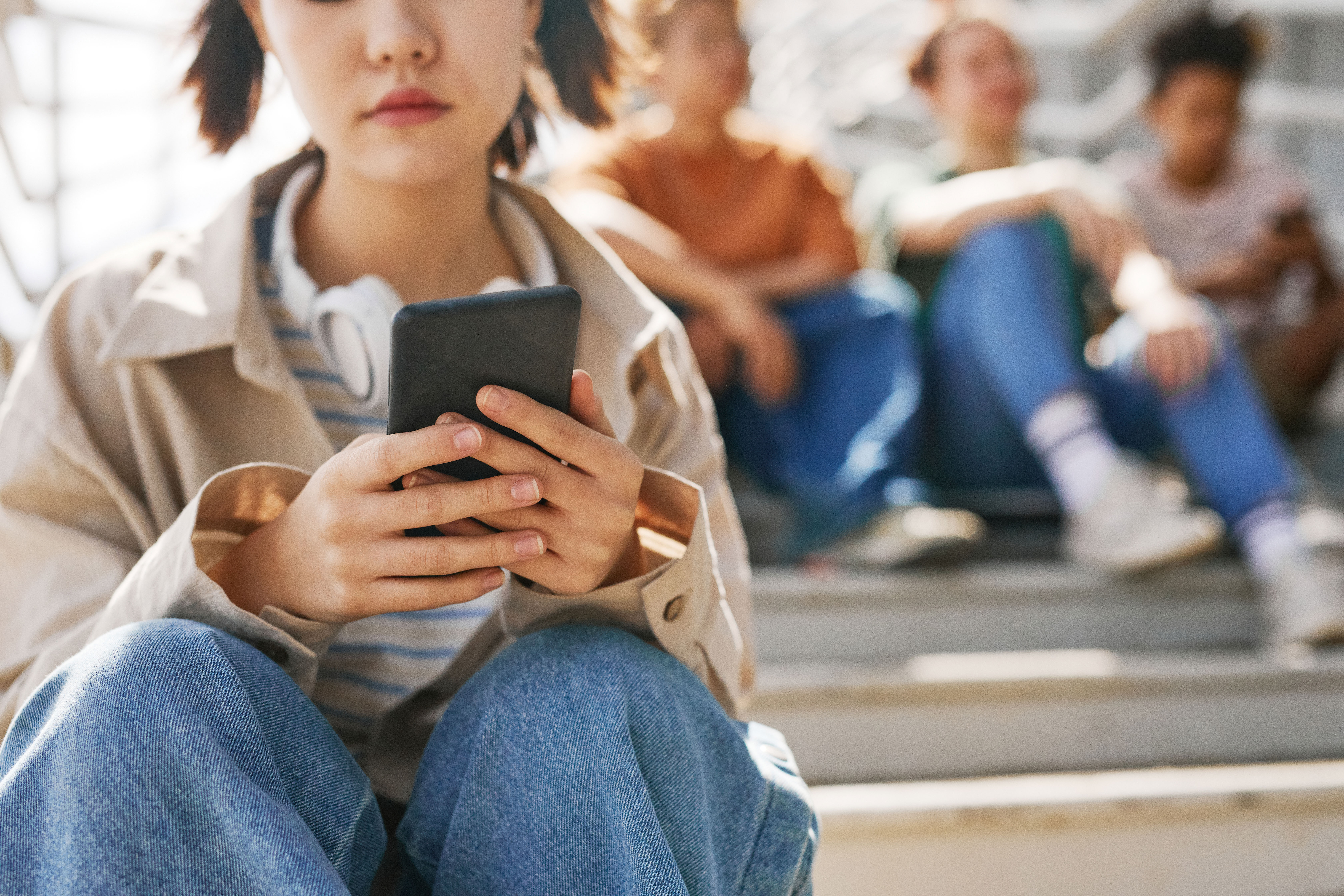 Girl on her phone sitting away from friends Girl on her phone sitting away from friends