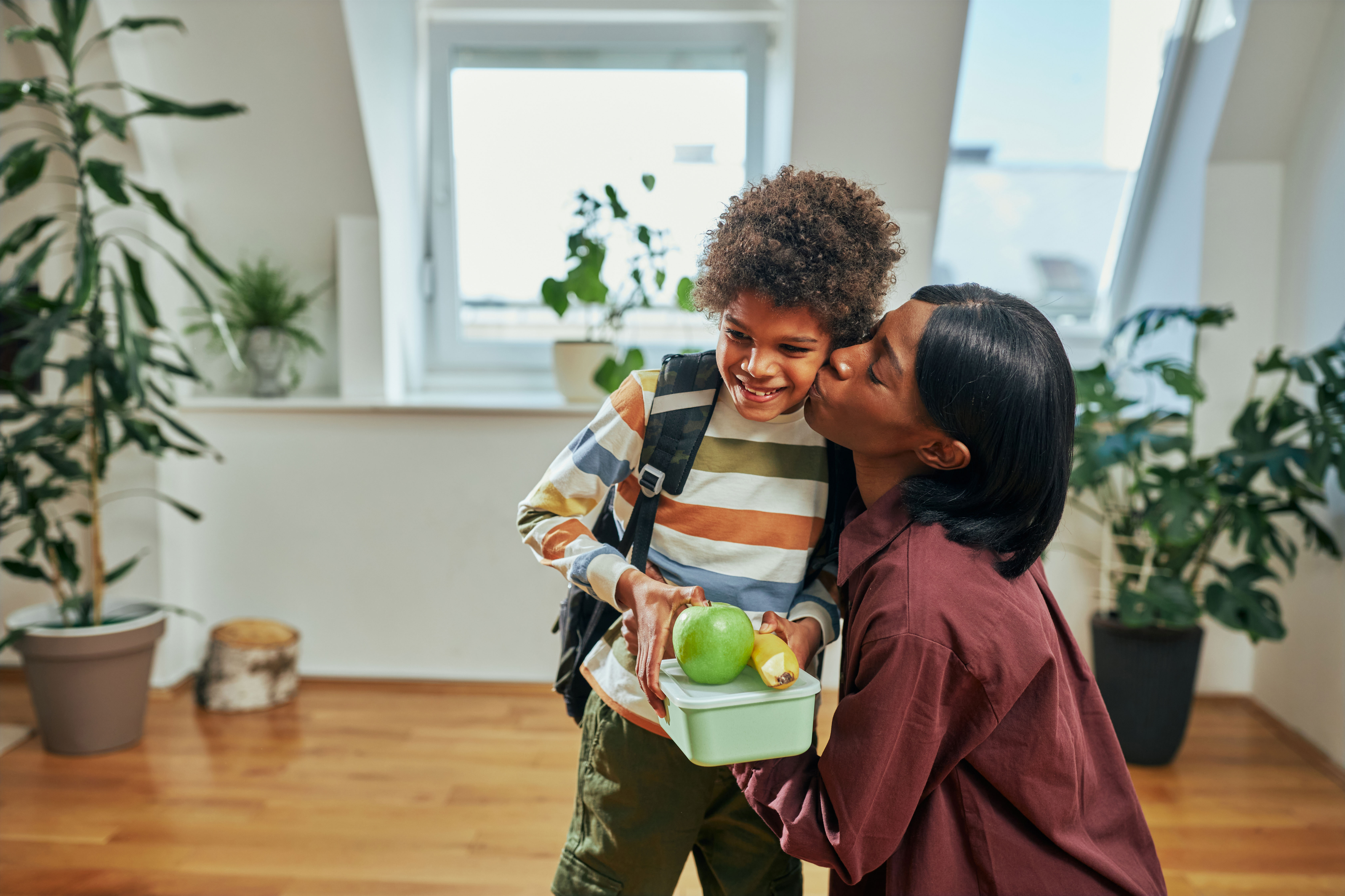 Mother kissing her son on cheek and handing him a healthy lunch