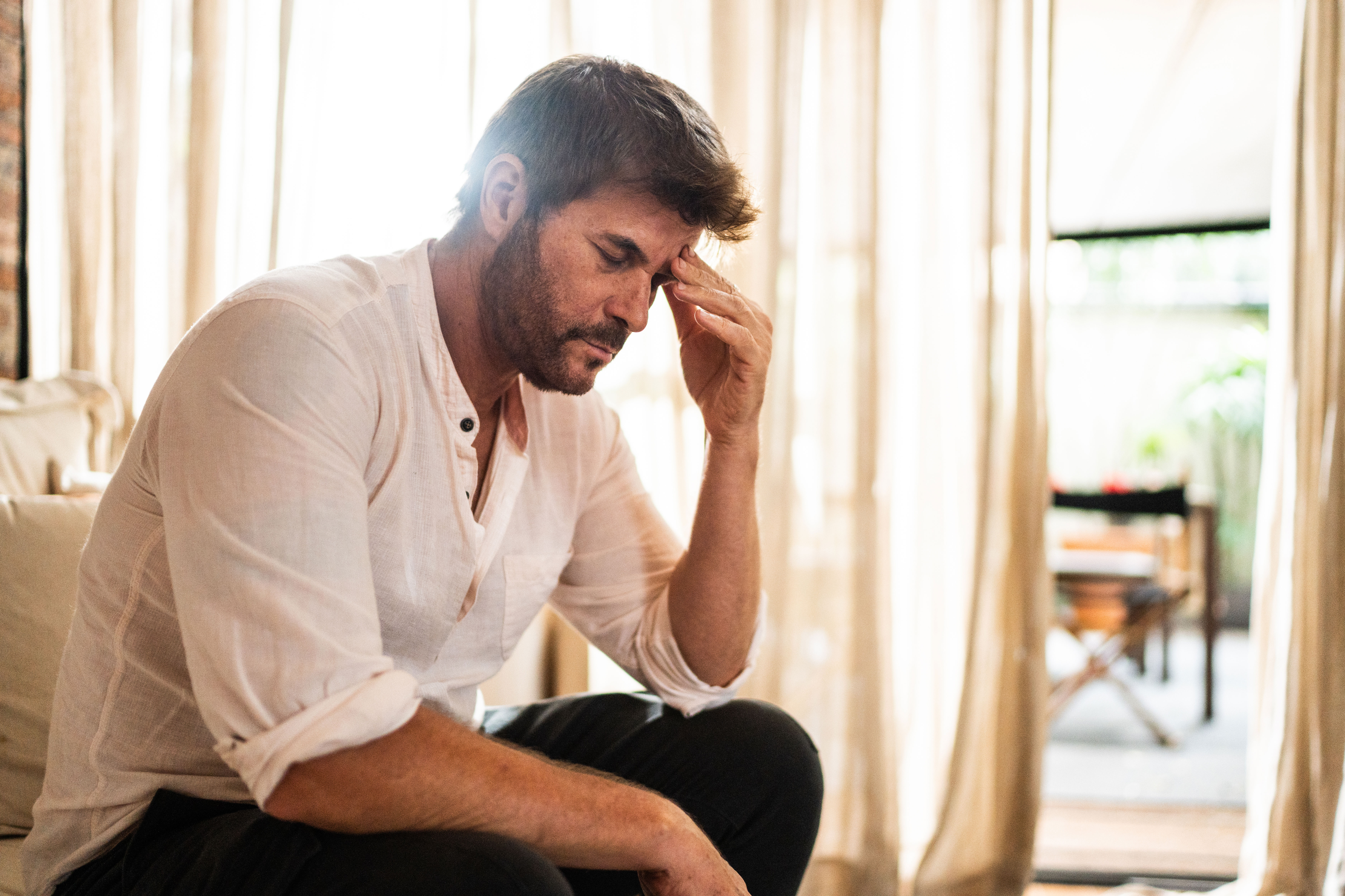 Man sitting on couch holding his head.