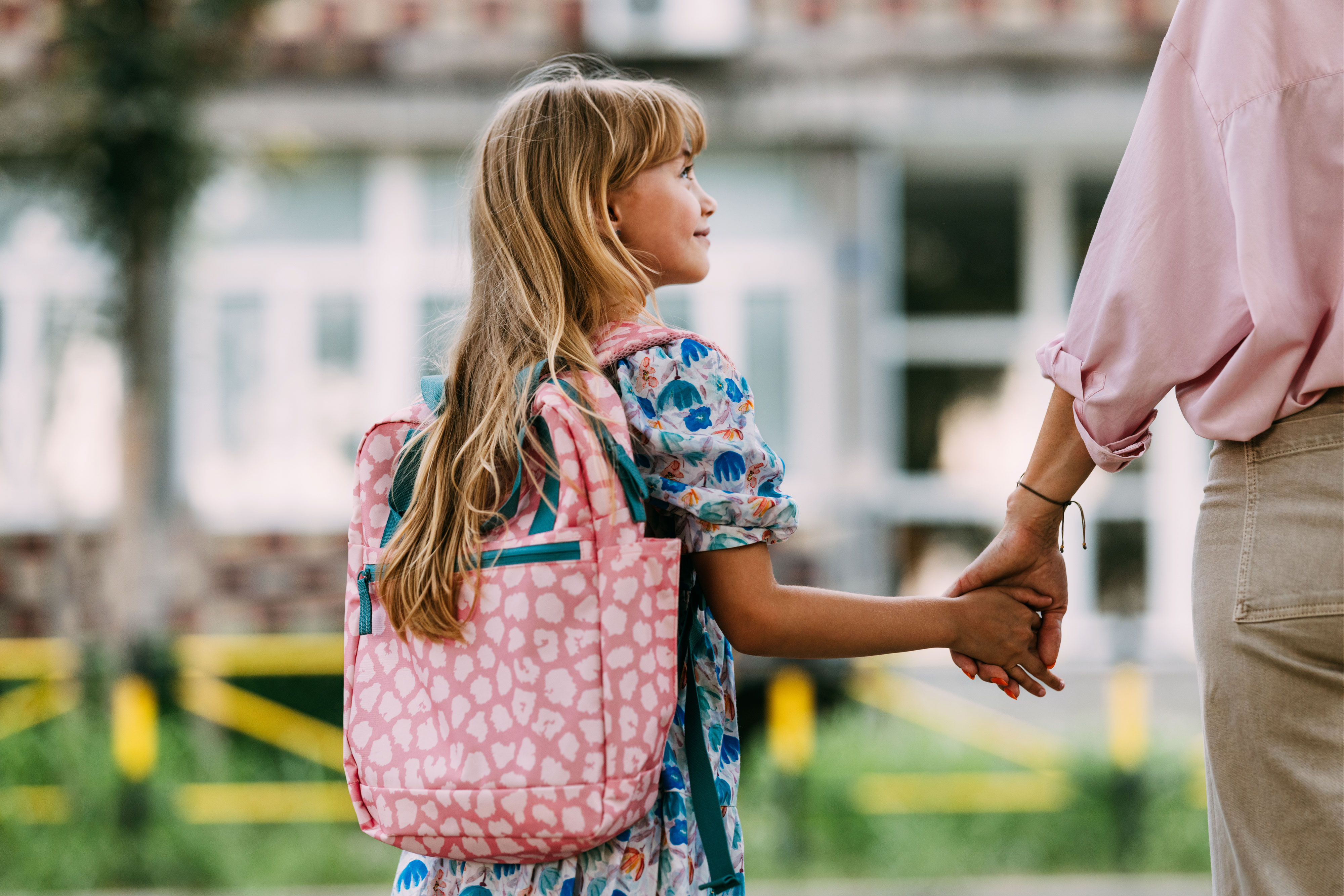 Young girl with backpack holding her parent's hand