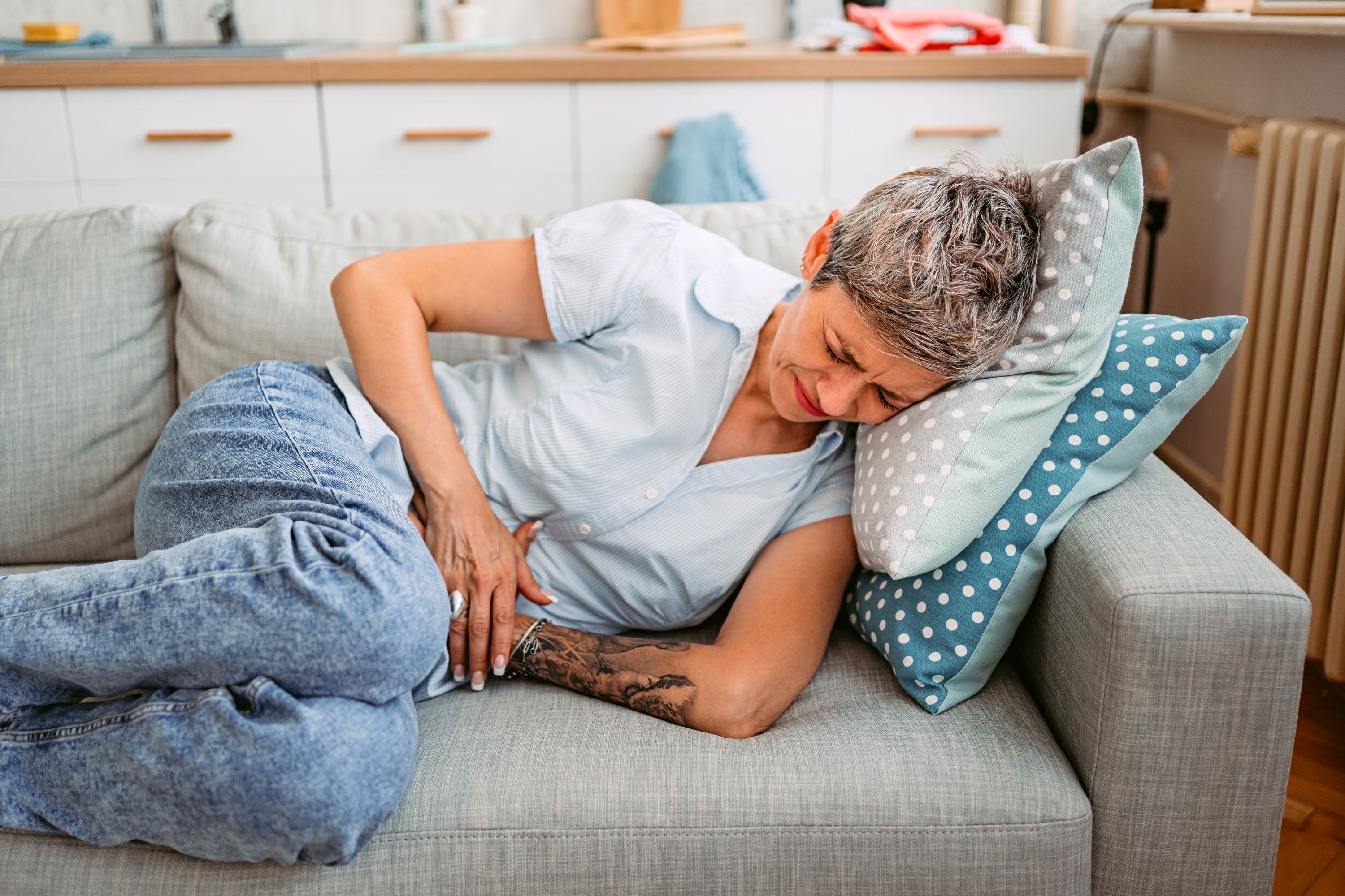 Uncomfortable woman laying on couch while clutching her stomach.