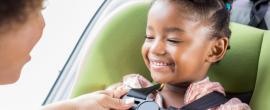 Parent buckles young girl into car seat