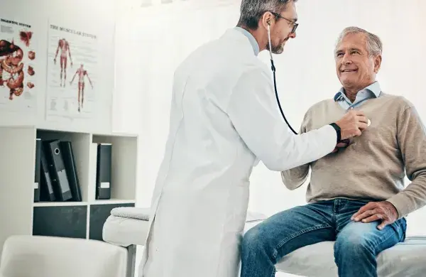 Doctor using stethoscope to listen to older man's heart