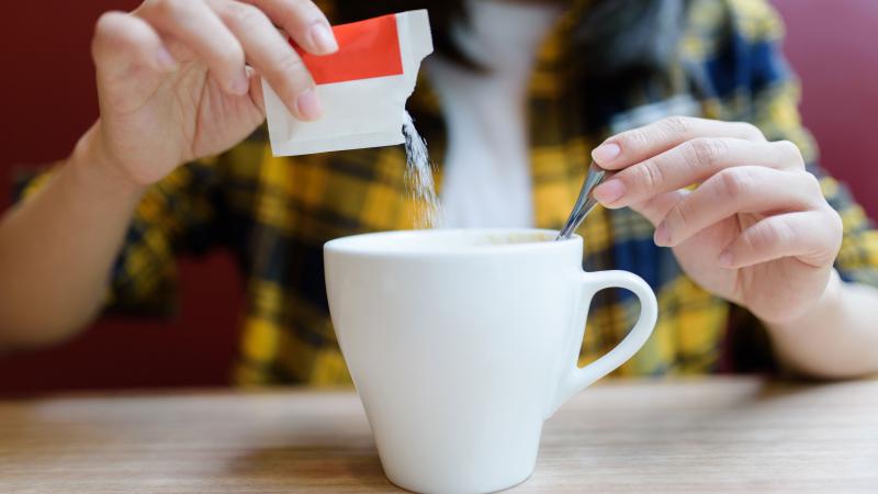 Person pouring sugar into a mug