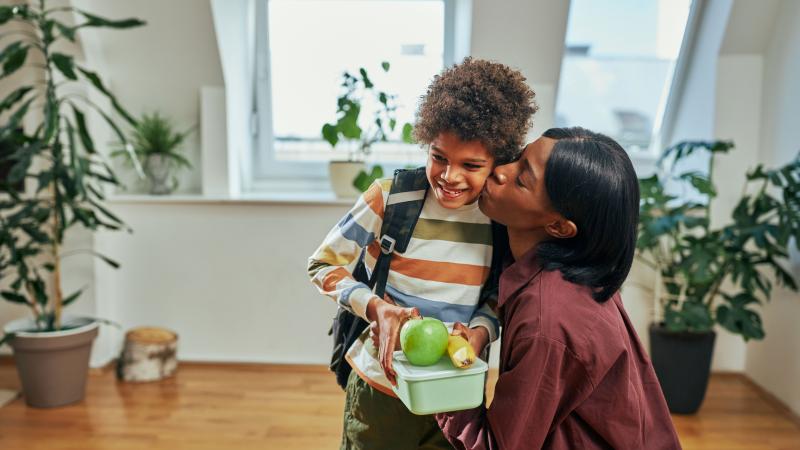 Mother kissing her son on cheek and handing him a healthy lunch