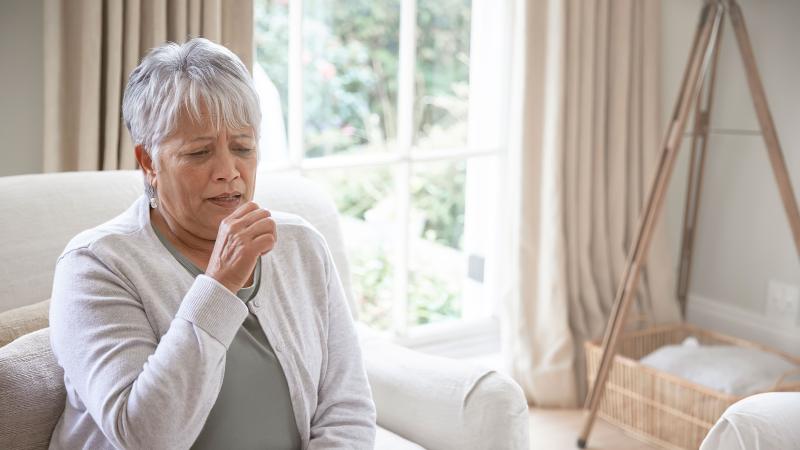 A senior woman coughing from symptoms of RSV.