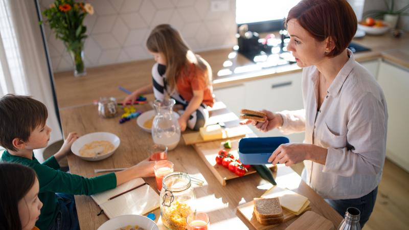 Mother of three little children preparing breakfast in kitchen at home