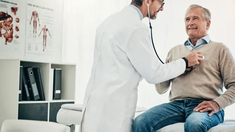 Doctor using stethoscope to listen to older man's heart