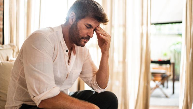 Man sitting on couch holding his head.