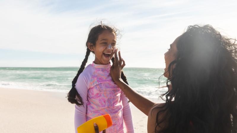 Mom putting sunscreen on daughter at the beach
