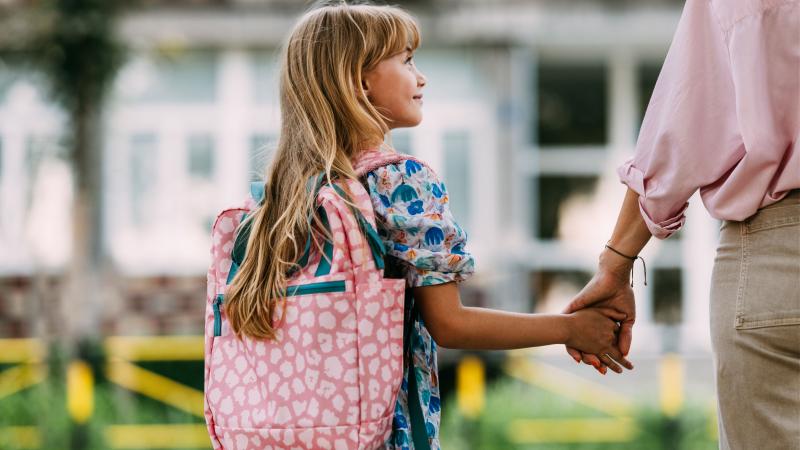 Young girl with backpack holding her parent's hand