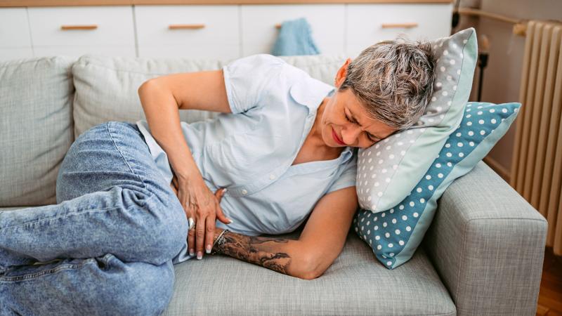 Uncomfortable woman laying on couch while clutching her stomach.