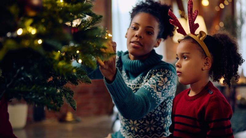 Mother shows child how to decorate Christmas tree
