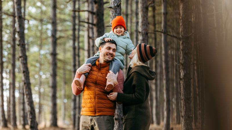 Child on father's shoulders with mother next to the father, in the woods