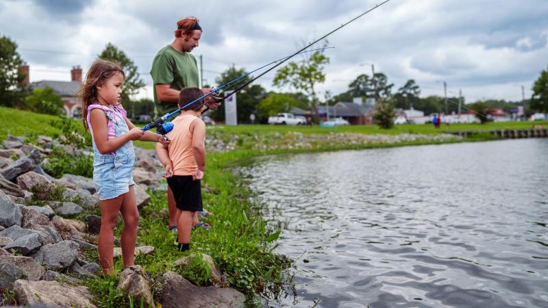 Two kids and an adult fishing at the edge of a small body of water