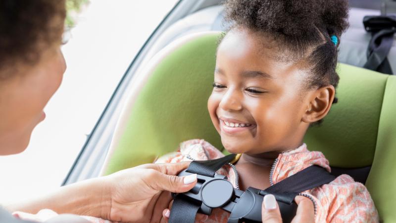 Parent buckles young girl into car seat