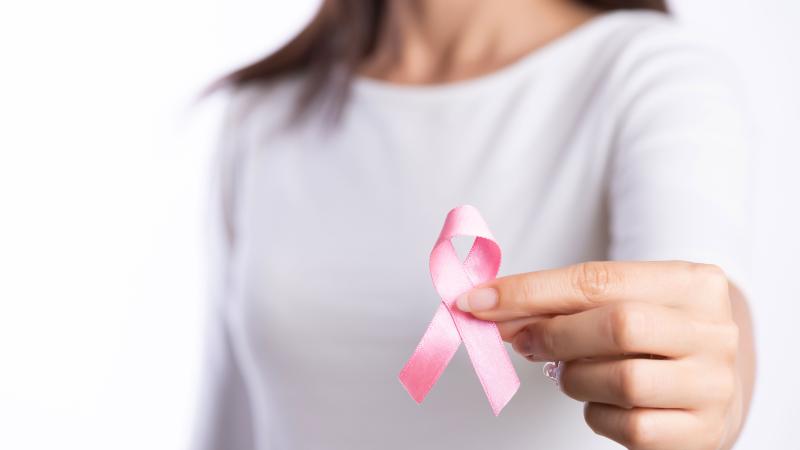 Woman holds up a pink ribbon for breast cancer; no face showing.