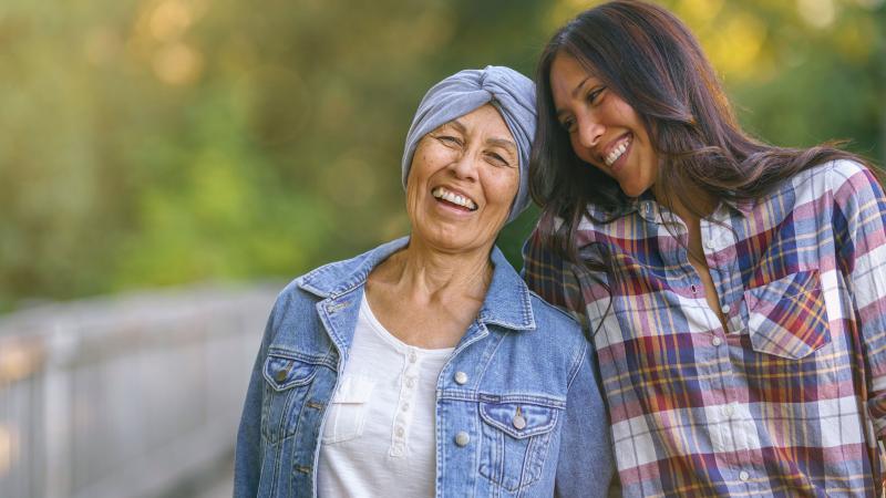 Mother with cancer and daughter smile while walking on a trail