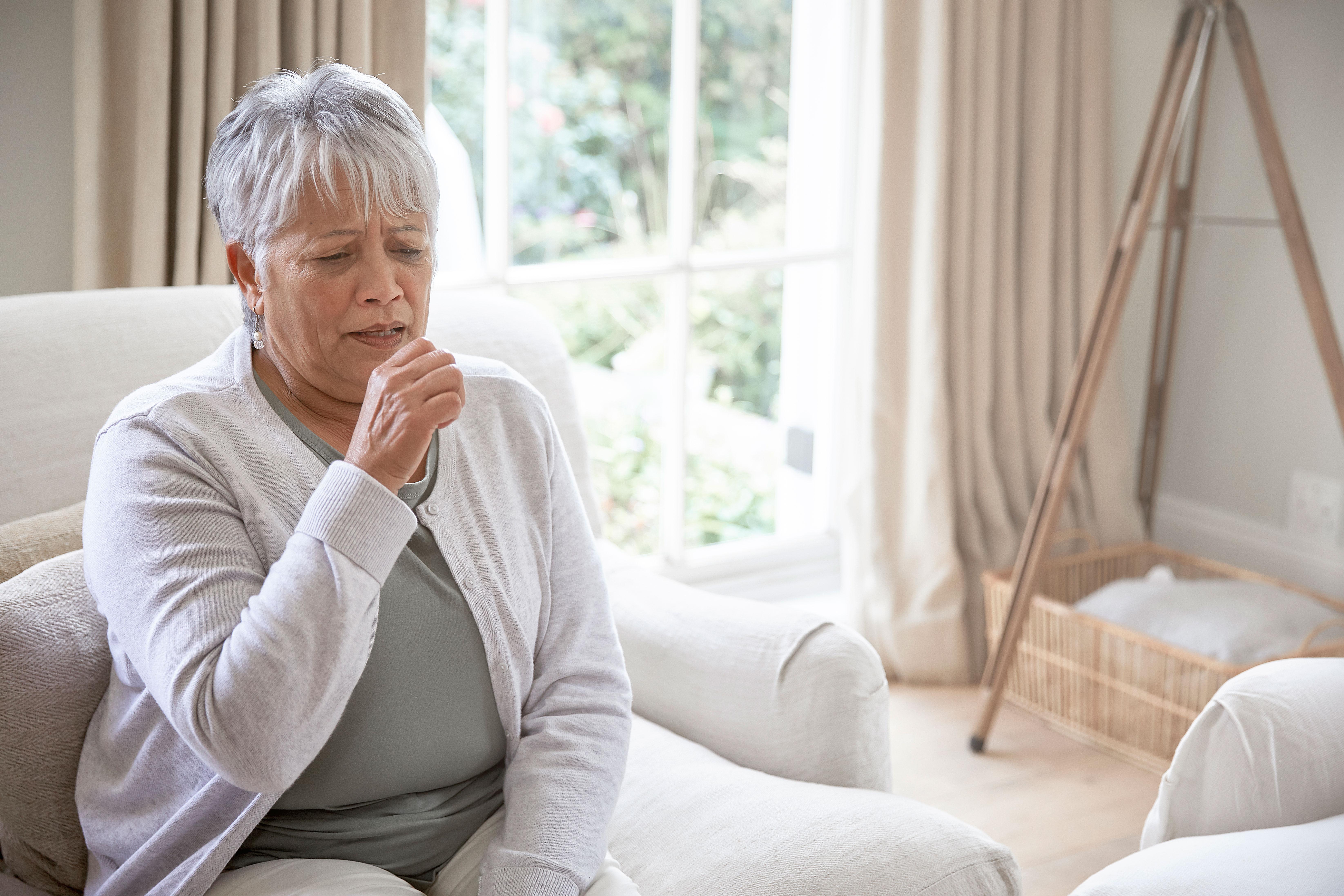 A senior woman coughing from symptoms of RSV.