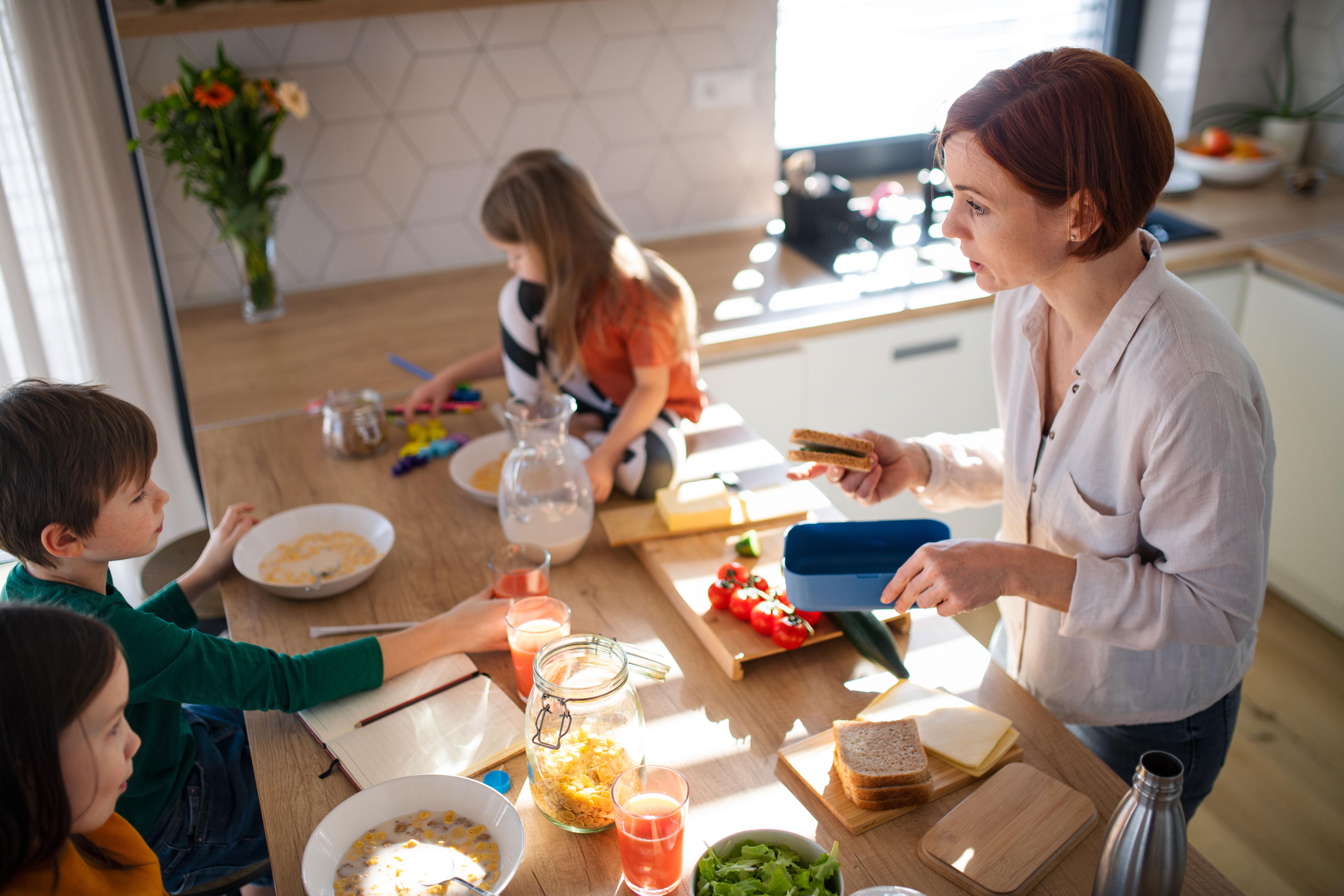 Mother of three little children preparing breakfast in kitchen at home