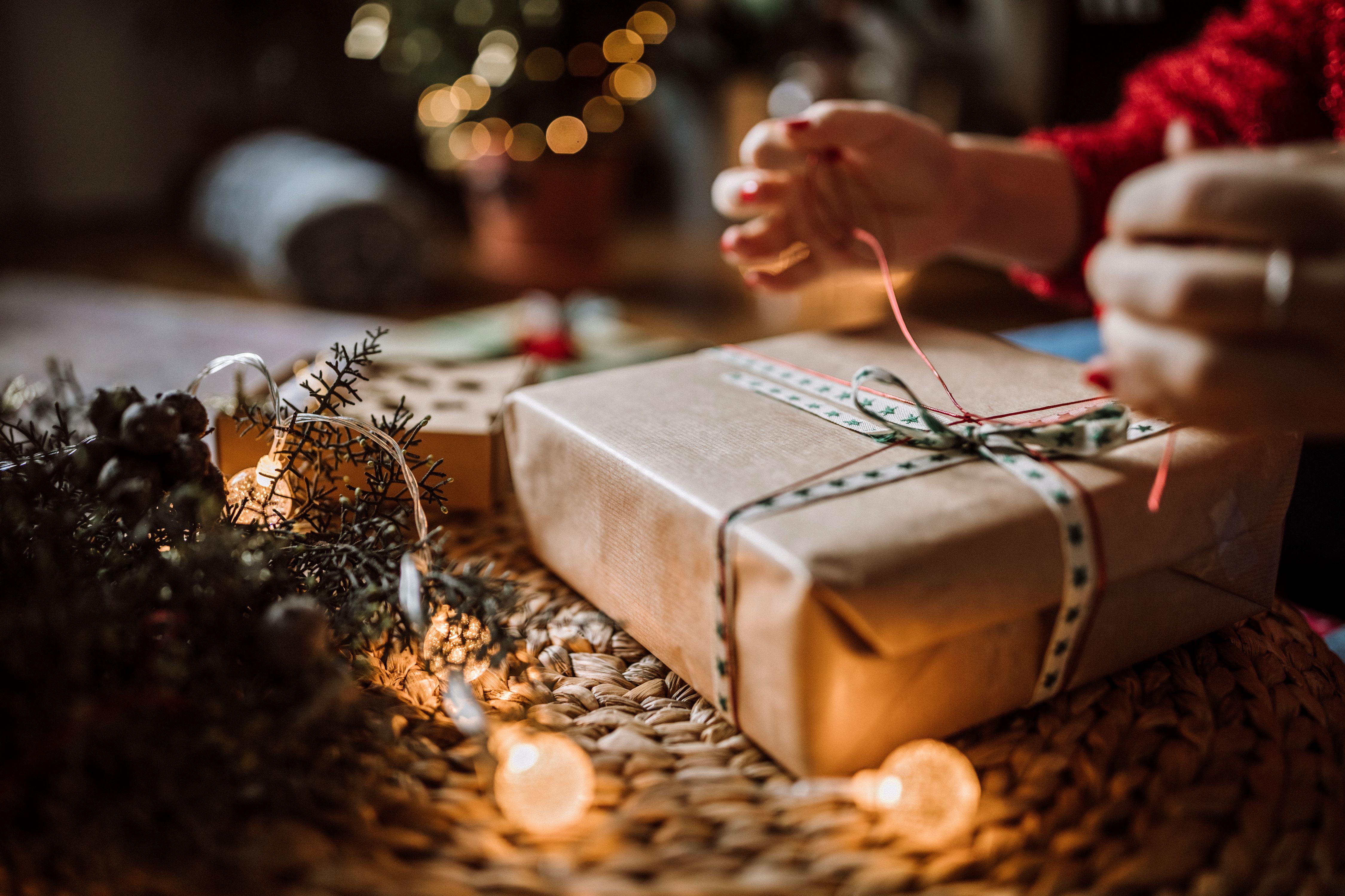 Person finishing wrapping a holiday gift by tying the bow