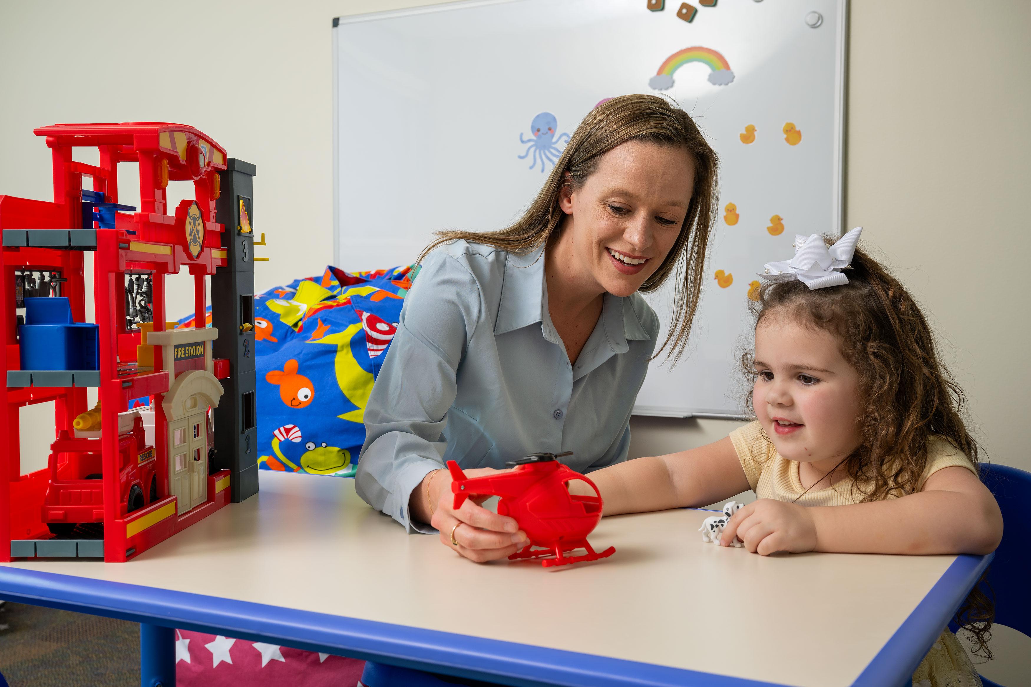 Therapist works with a child, showing the child a toy.