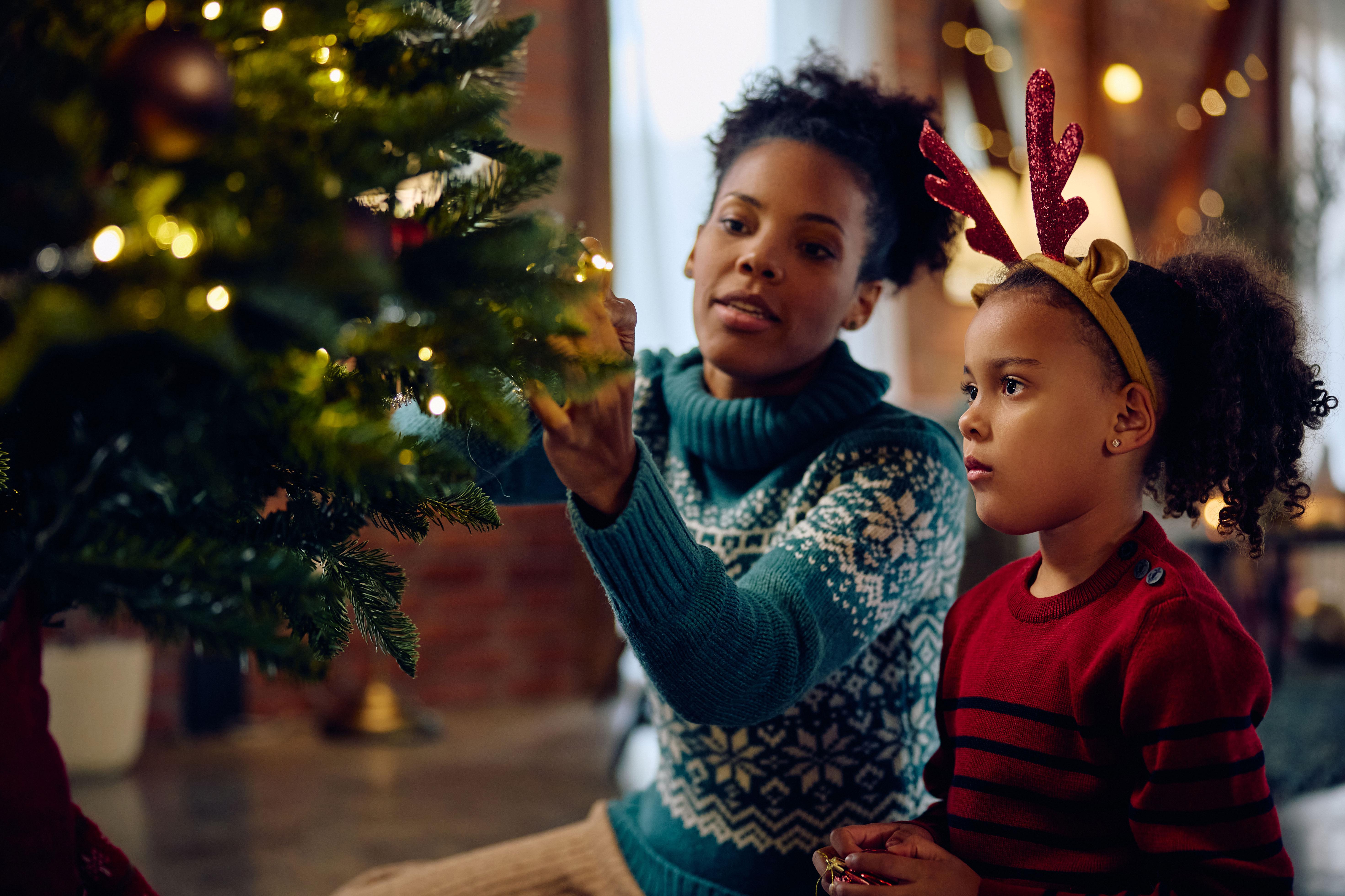Mother shows child how to decorate Christmas tree