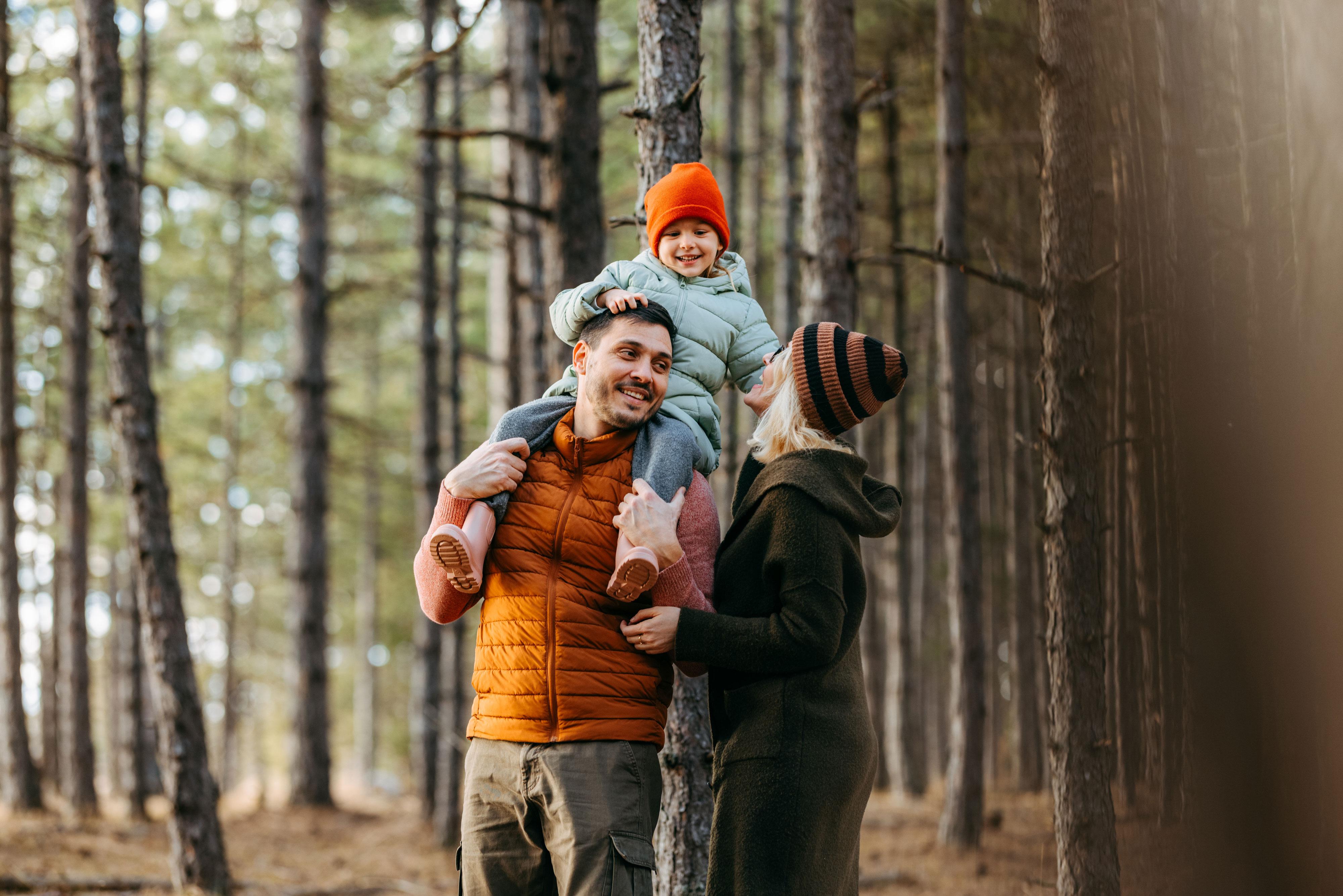Child on father's shoulders with mother next to the father, in the woods