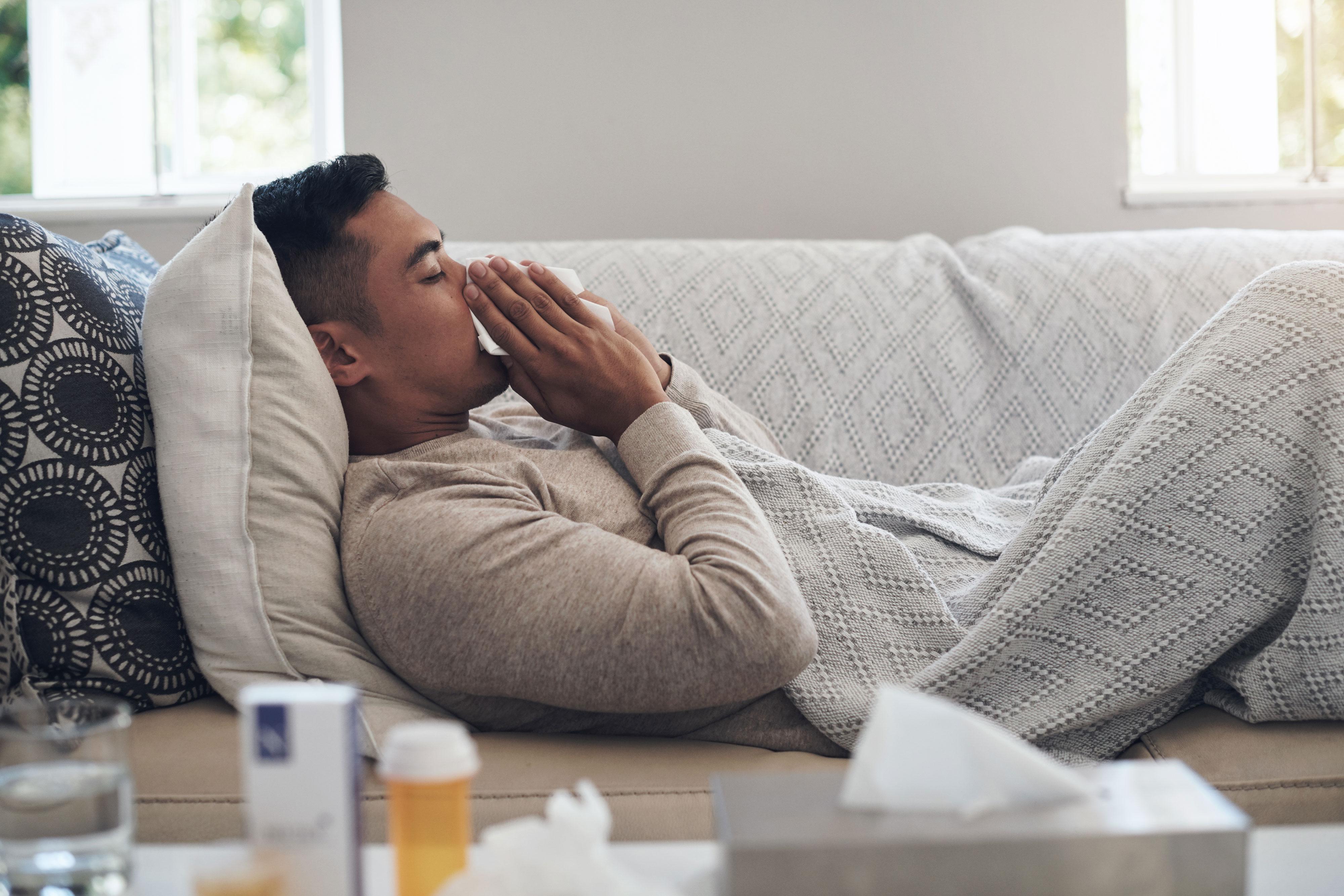 Sick man blows his nose while laying on the couch