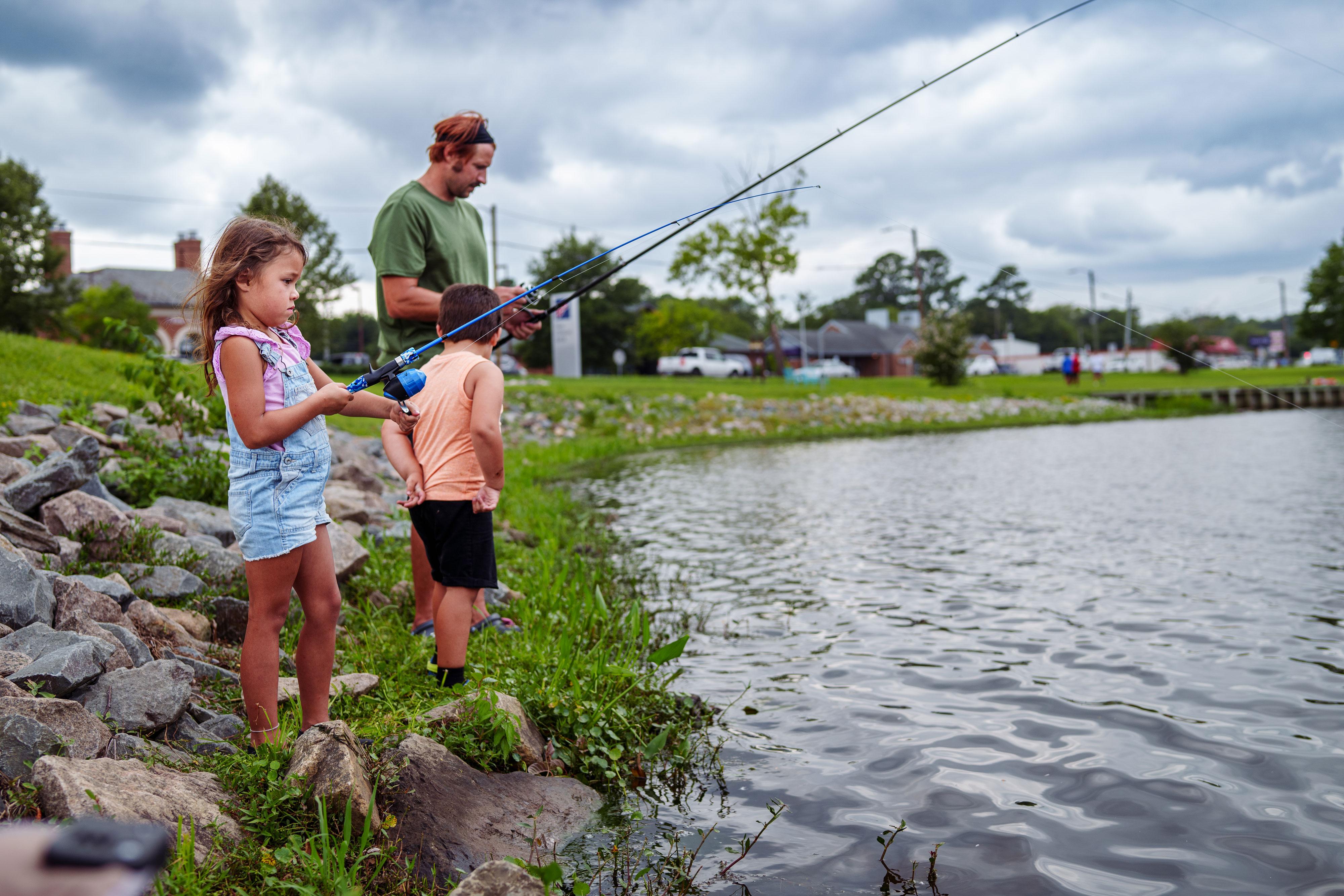 Two kids and an adult fishing at the edge of a small body of water