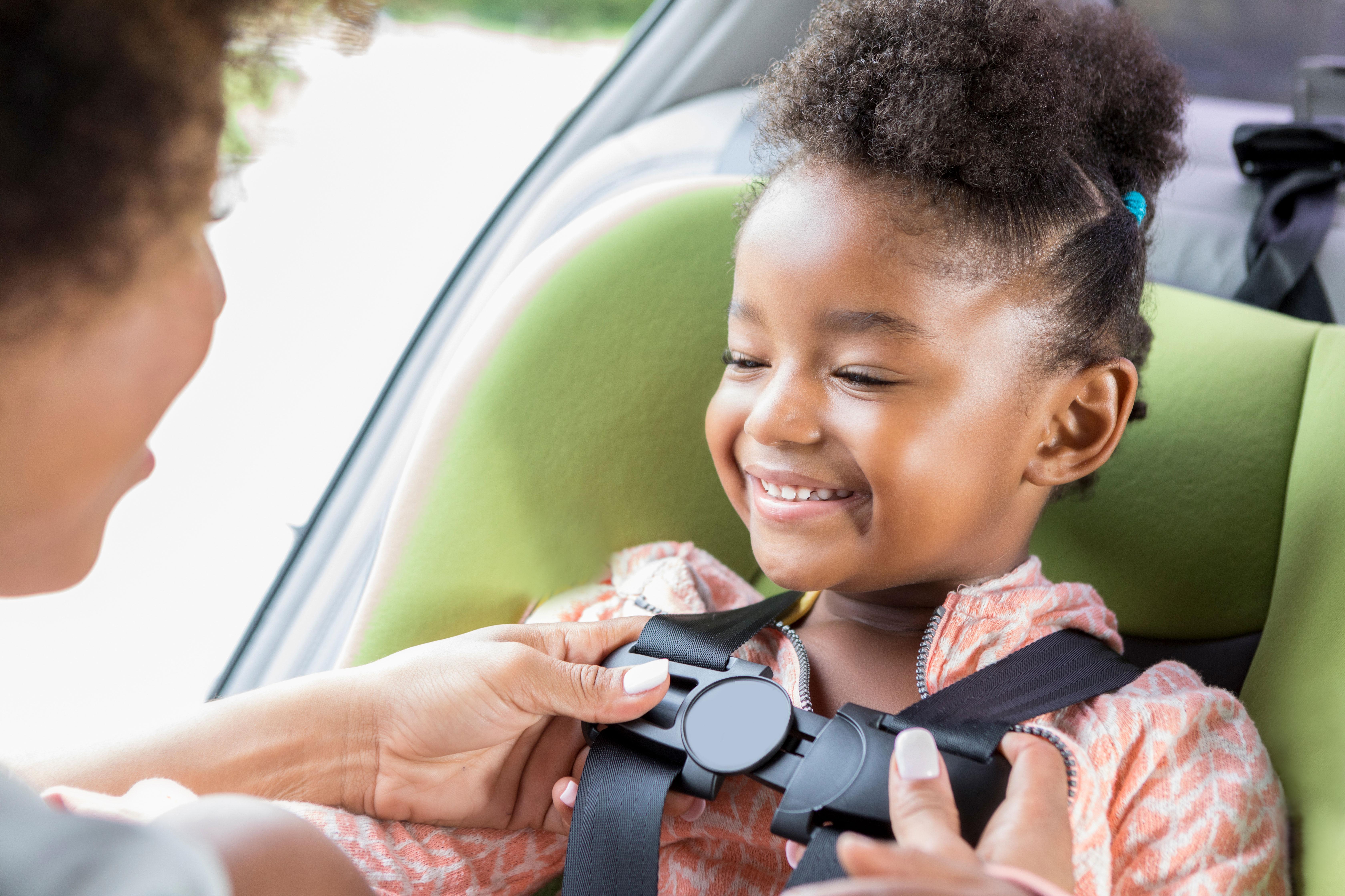 Parent buckles young girl into car seat