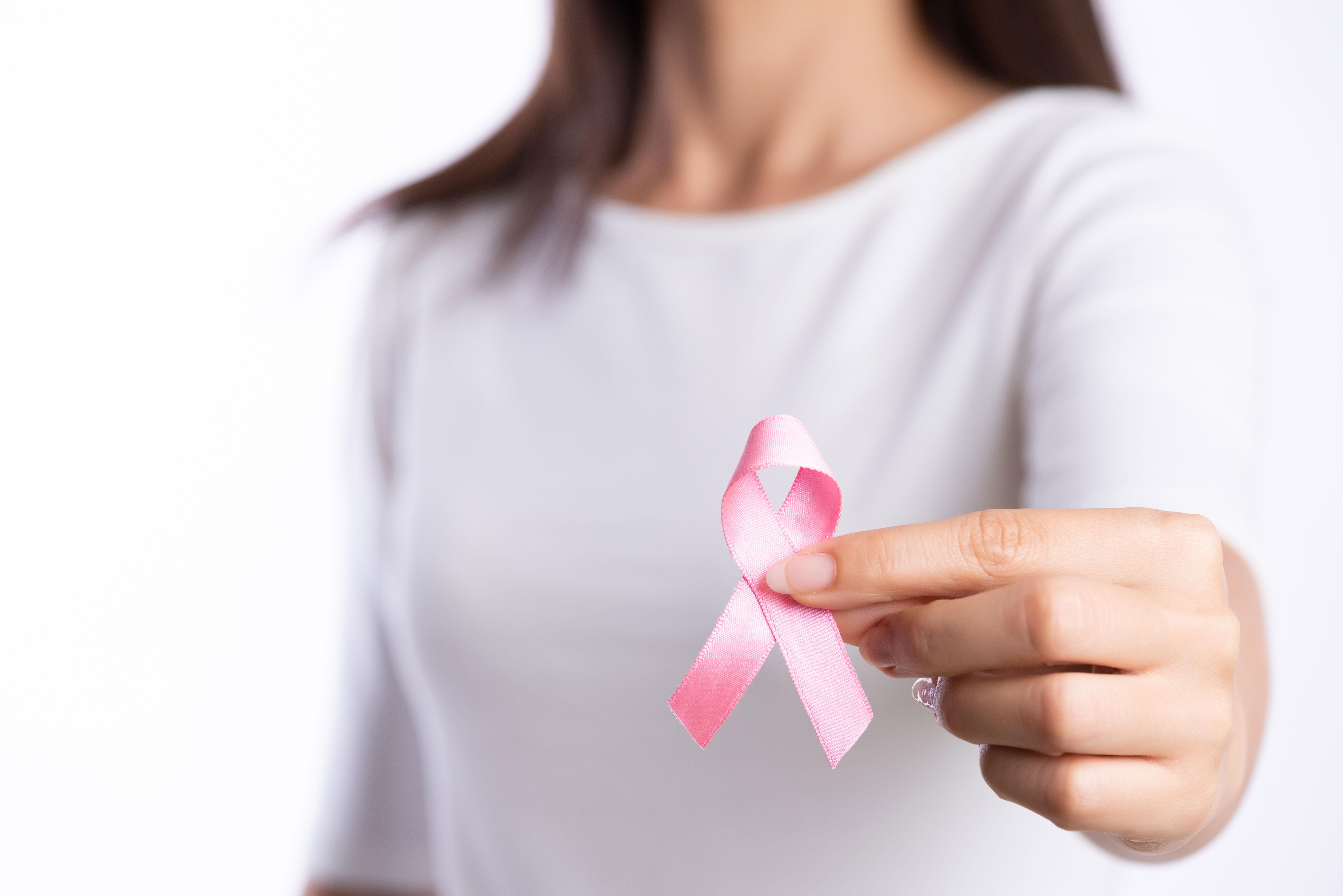 Woman holds up a pink ribbon for breast cancer; no face showing.