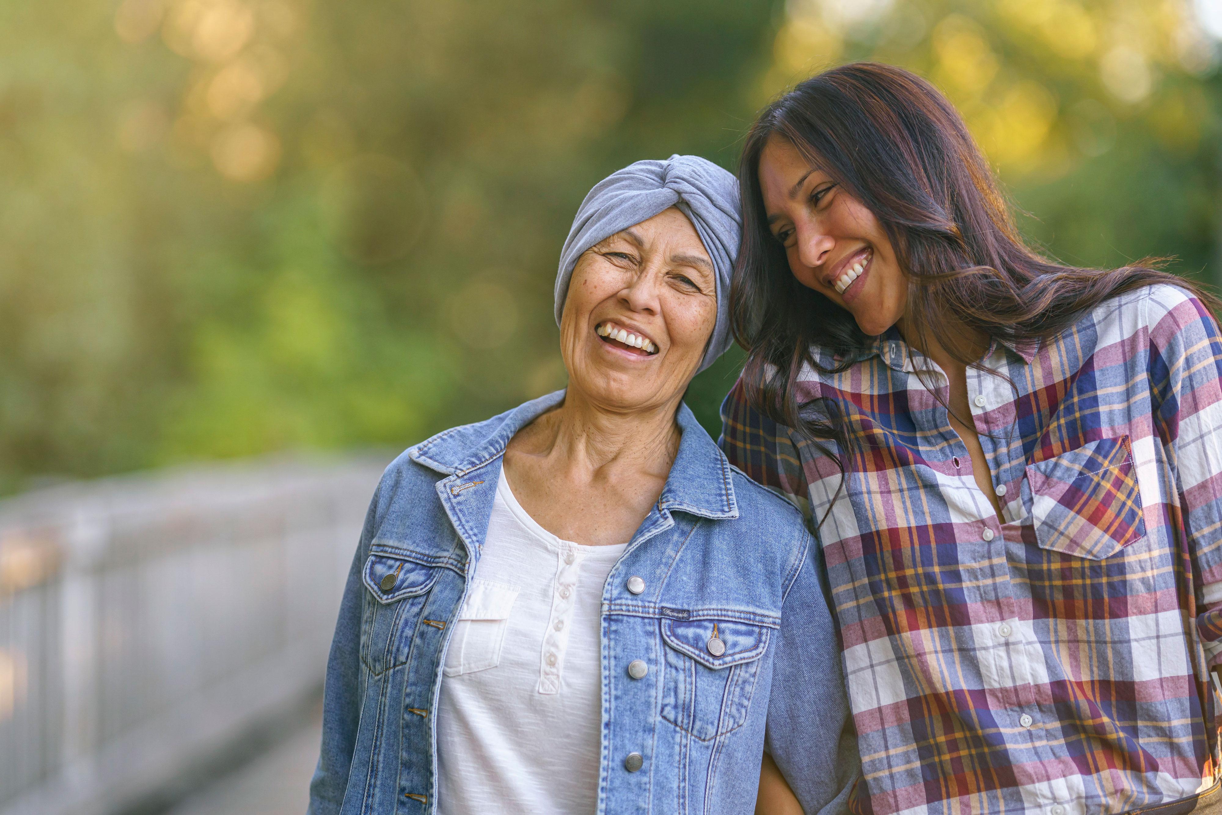 Mother with cancer and daughter smile while walking on a trail