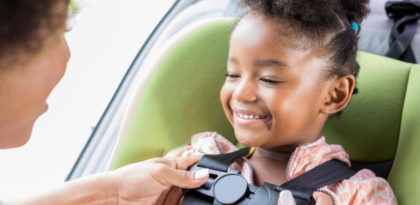 Parent buckles young girl into car seat