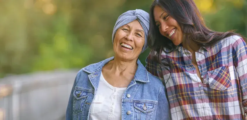 Mother with cancer and daughter smile while walking on a trail